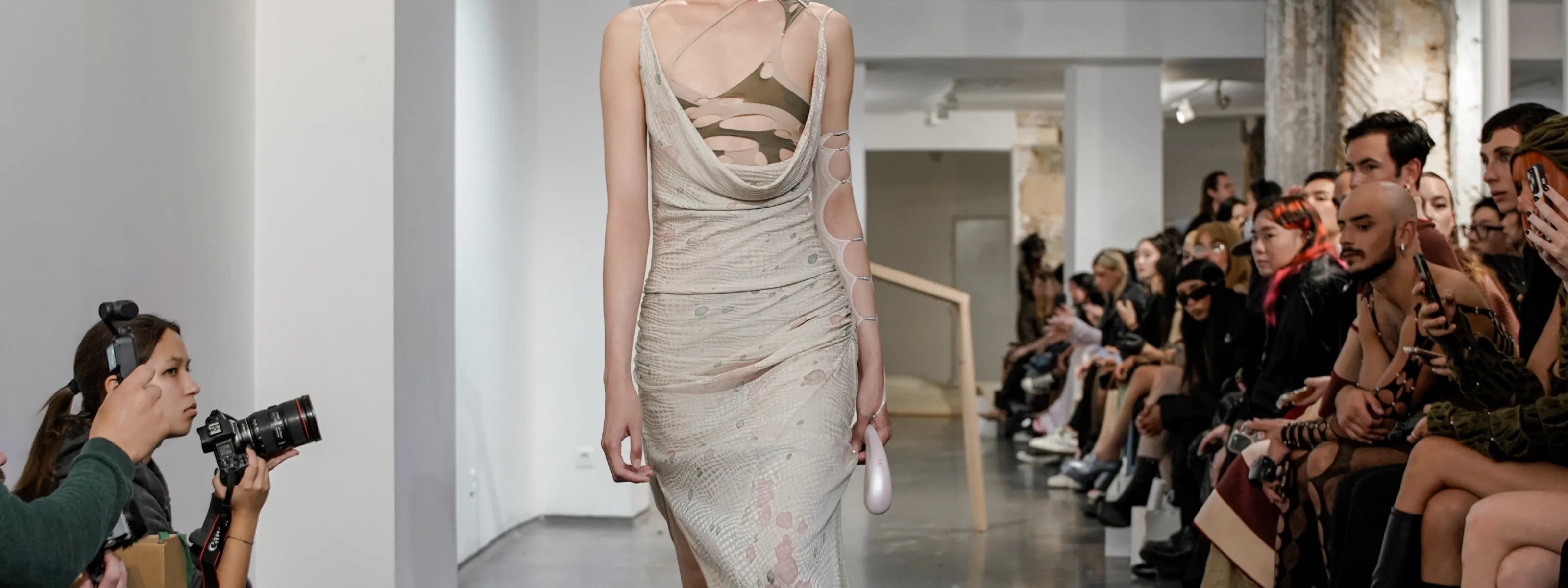 Model walking down a runway at a paris fashion show with an audience on either side.